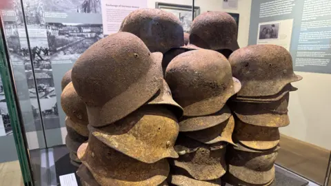 Rusty WWII German Troops helmets, stacked up and on display in a glass case in the new Liberation exhibition.