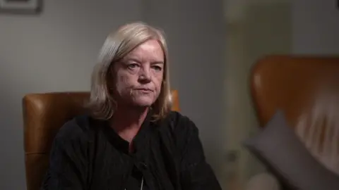 Baroness Casey in a tan leather armchair looking slightly off camera. She has blonde hair and is wearing a black blouse