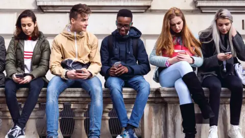 Getty Images Teenage boys and girls sitting together using their phones