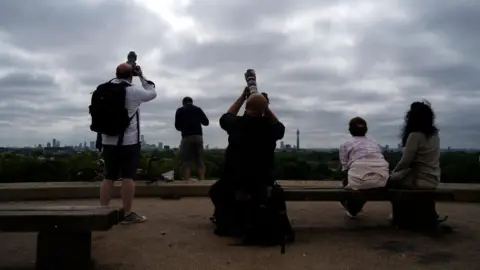 Getty Images People watch the sky from Primrose Hill in north London as photographers aim cameras towards the horizon.