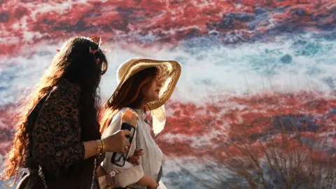 Two women and a man walk past a billboard showing an artistic impression of clouds in the red, white and blue colours of the US flag.
