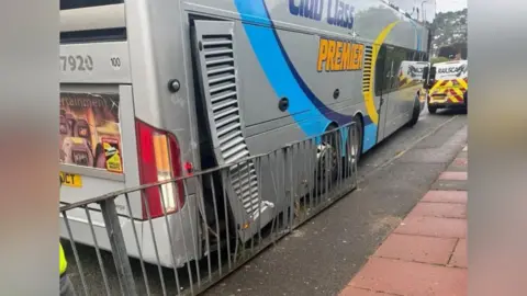 Supplied A grey bus with a panel hanging off the side of it. It is next to some damaged railings.