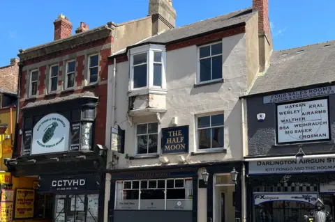 A pub, painted white, on a street with shops either side.