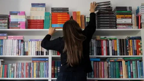 A woman reaches up to take Russian-language books from a shelf