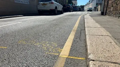Tracey Cahill/ BBC A slight depression on a two lane road with stone paving slabs. There are some yellow lines marking an issue on the road surface.