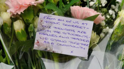 PA Media A handwritten note on a bouquet of flowers. It reads: "From all of us at Young Somerset - our thoughts are with the students, families and teachers. We stand together as a community x"
