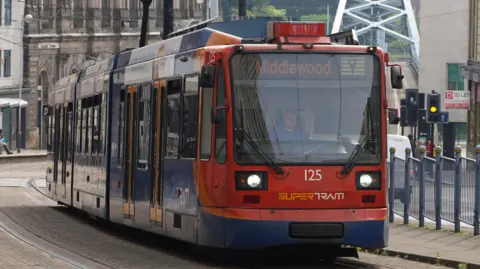 A tram in Sheffield city centre. It is red, orange and blue and displays its destination as 'Middlewood'.