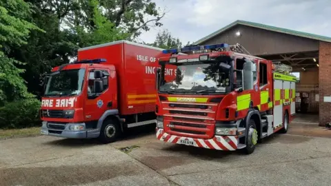 A fire engine and fire service lorry parked on concrete forecourt outside East Cowes fire station