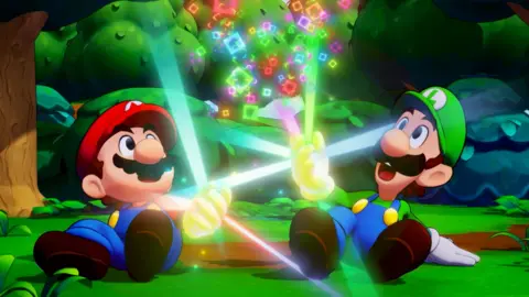 Nintendo Mario and Luigi, wearing their famous blue overalls and coloured caps, sit on the ground. Each is looking upwards with a shocked expression as a magical yellow glow emanates from their hand, creating a cascade of colourful squares between them.