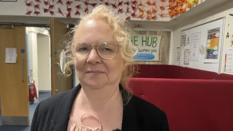 Jo Whiteside - a blonde woman in glasses and a blazer - stands in a school room.