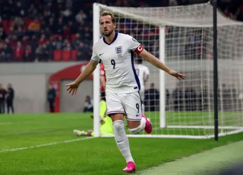 Getty Images Harry Kane dressed in England kit celebrates a goal with his arms outstretched and in the background is a goalkeeper slumped on the ground in front of a goal net. It's a World Cup qualifier against Albania in Tirana in 2025
