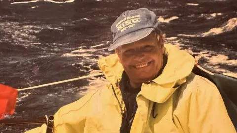 Victor Tinley is pictured in an old photograph. He is on a boat, smiling at the camera. He is wearing a yellow waterproof and blue cap.