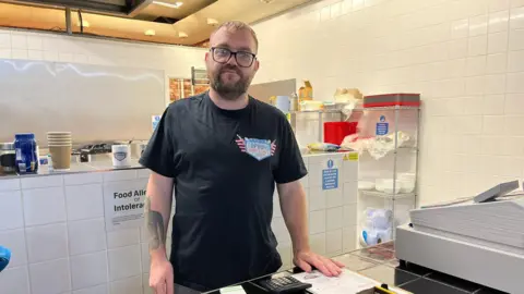 Chris stands in his kitchen and looks at the camera