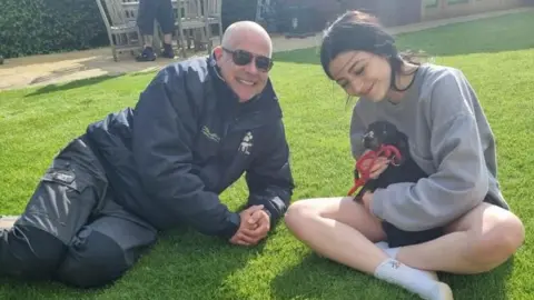 Family photo Phil James and Alannah sitting on grass with a dog