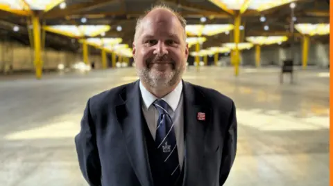 Swindon Borough Council A man in a suit and tie standing in an empty warehouse building looking at the camera.