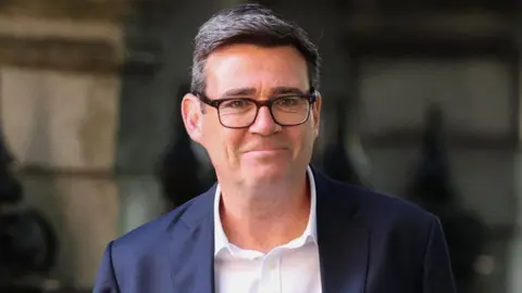 A headshot of Andy Burnham in a blue jacket and white shirt.