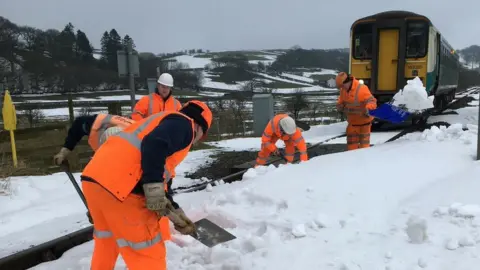 @ArrivaTW/Twitter Railway workers clear snow from the Heart of Wales line