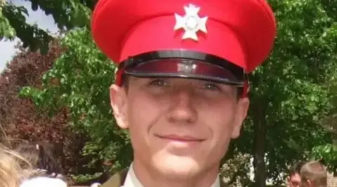 Family photo A man in a red army-style cap, with a black beak and a silver cross in front of a green bush