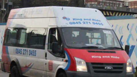 A mainly white bus fills most of the screen. It has the words Ring and Ride and a phone number in blue above the windscreen.