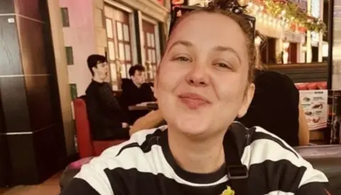 Jenni Hayes sitting in restaurant in black and white striped jumper eating hamburger