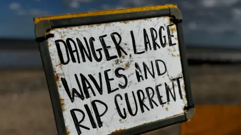 Crispin Rolfe/BBC Sign on the promenade which reads: "Danger large waves and rip currents."