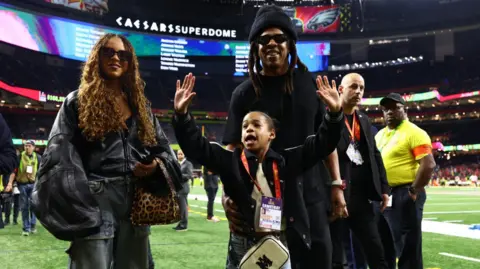 Reuters Blue Ivy wears an oversized leather jacket paired with casual cargo denim; while standing next to her father Jay Z and sister Rumi

