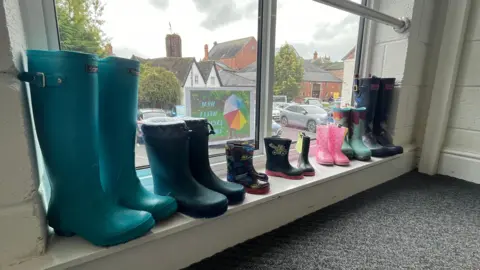 Seven pairs of wellies of varying sizes and colours lined up on a windowsill