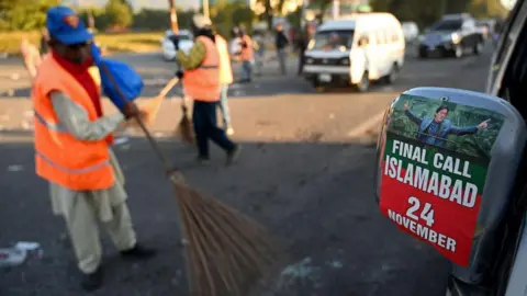 Getty Images Municipal workers clean a road leading to a Red Zone area near damaged vehicles after an overnight operation by security forces against supporters of Imran Khan's jailed Pakistan Tehreek-e-Insaf (PTI) party in Islamabad on November 27, 2024. 