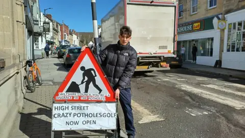 Ben Thornbury with pothole sign on pedestrian crossing