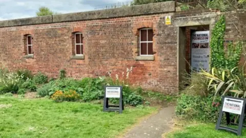 National Poo Museum One storey brick building with three windows and a door with A-frame signs outside.