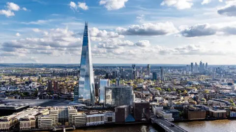 An aerial photo looking south from the River Thames - the Shard is prominent in the front of the image and low hills are visible in the distance.