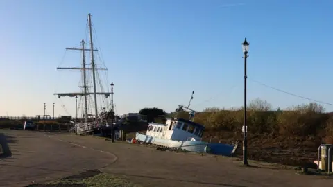 SOSE Two boats by the quayside. One is upright but a second - in the foreground - is tilting to the right. 