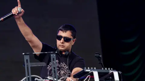 Panjabi MC stood behind a dj deck on stage performing
