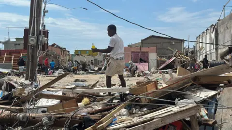 Brandon Drenon / BBC A man is seen looking through debris for food and water