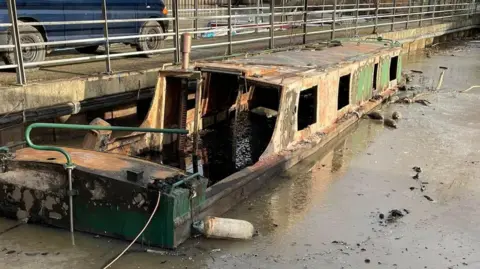 The shell of a moored narrow boat, showing considerable fire damage to the inside and out.