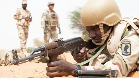 A US Airborne division soldier in camouflage and wearing a helmet lies on the ground pointing a gun during joint multinational exercise African Lion 2025 in Dodji, Senegal - May 2025.