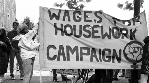 Beezer A young woman demonstrating over wages with a banner reading wages for housework campaign.