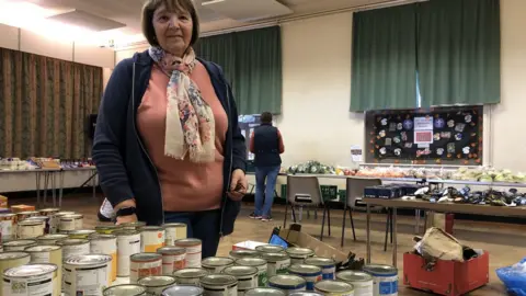 Jon Wright/BBC A woman standing behind a table of food in a church hall