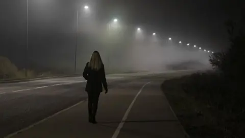 Getty Images Woman walking along street lit by street lights