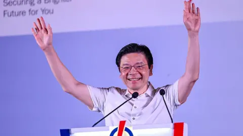 Singapore PM Lawrence Wong smiles with both his arms held aloft as he addresses a crowd at an election rally 