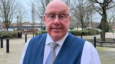 Man in waistcoat and tie stood outside