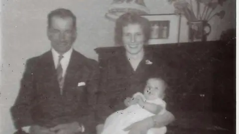 Armstrong family A black-and-white photograph of Bob and Margaret Armstrong. Bob is wearing a suit and tie with a handkerchief in his top pocket, while Margaret has a dress with a broach on the lapel and is holding a baby