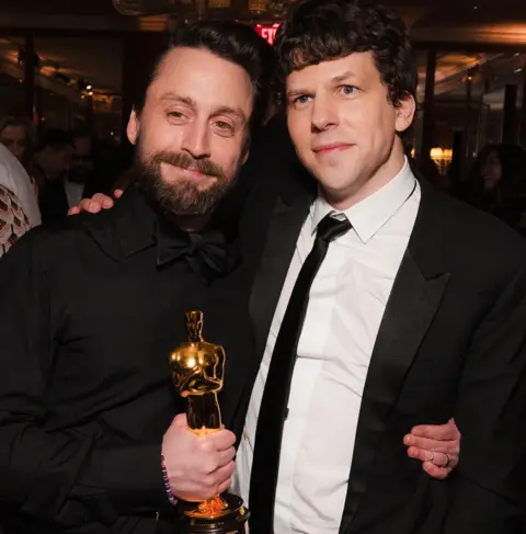 Getty Images Kieran Culkin holding his Oscar, standing with an arm around Jesse Eisenberg