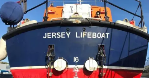 Jersey Lifeboat Association The front of a blue and red vessel with Jersey Lifeboat written on it. 