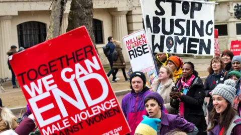 Getty Images Women hold placards as they take part in Million Women Rise march through central London to New Scotland Yard in a protest demanding an end to male violence against women and children ahead of International Women's Day on 5 March 2022