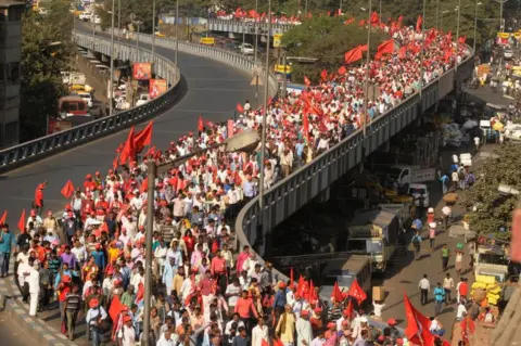 Getty Images Farmers wave flags and raise slogans as they participate in a protest march organised by Left Front from Singur to Raj Bhawan over their various demands, at Howrah Bridge crossing, on November 29, 2018 in Kolkata, India.