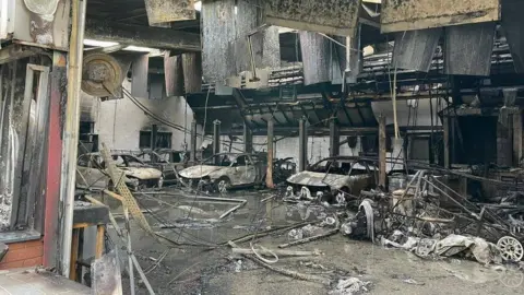 Devon & Somerset Fire & Rescue Service view of a burnt out motor workshop with twisted metal and fire damaged cars