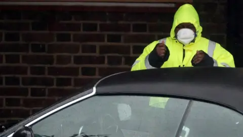 Reuters A security guard wears a surgical mask as he assists a car at a Coronavirus drive-through test centre at Parson"s Green Medical Centre in London