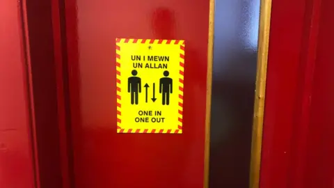 A sign on a toilet door reading 'one in, one out'