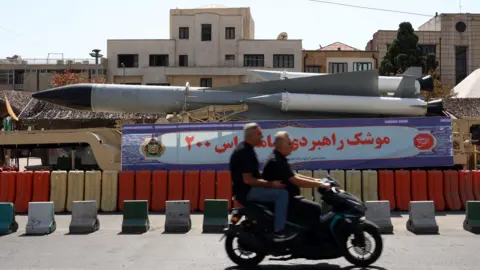 EPA Iranians drive past a missile on display in Baharestan Square in Tehran, Iran, during Defence Week (24 September 2024)